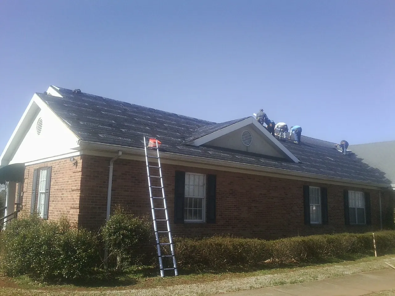 Crew tearing shingles off a brick ranch roof with a ladder set — Emergency Roof Repair work by our crew in Atlantic